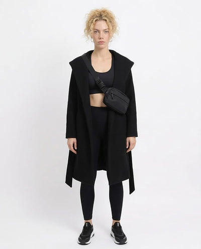 Person wearing a black coat, black top, and black leggings with a black bag on a white background