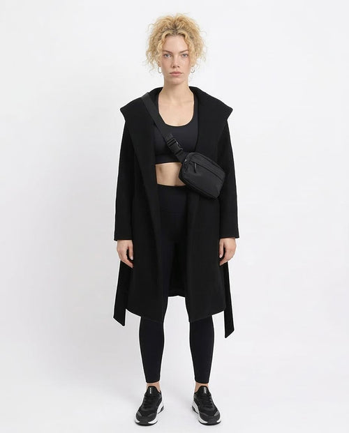 Person wearing a black coat, black top, and black leggings with a black bag on a white background