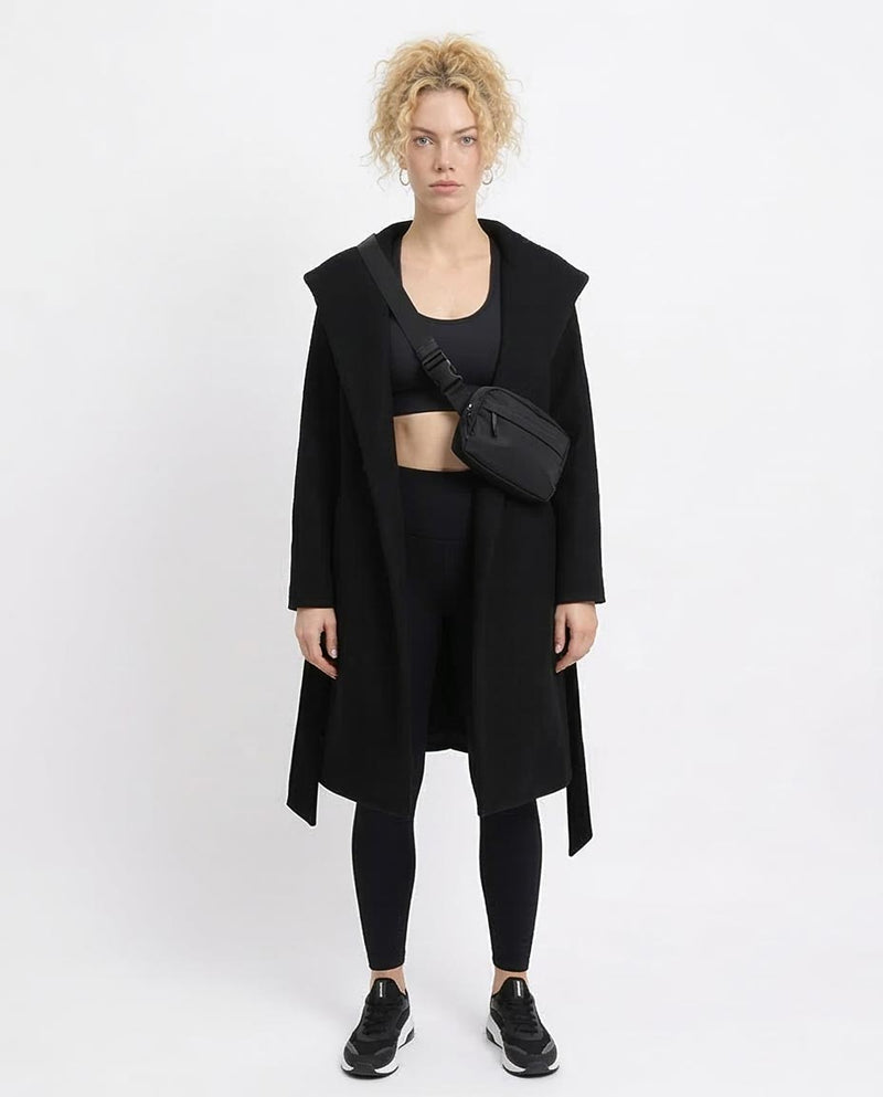 Person wearing a black coat, black top, and black leggings with a black bag on a white background