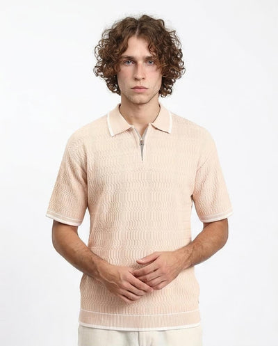 Man wearing a beige knitted polo shirt against a white background