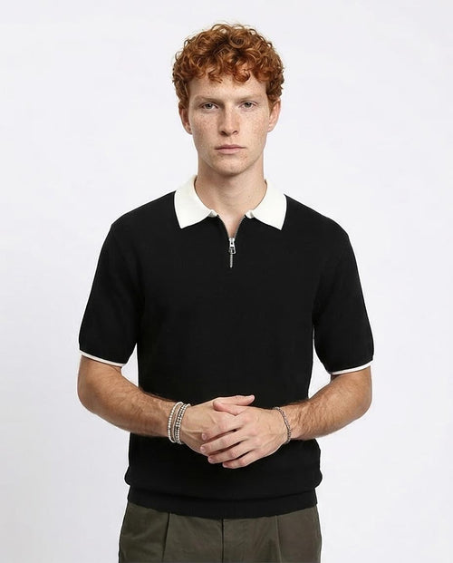 Man wearing a black polo shirt with a white collar against a plain background