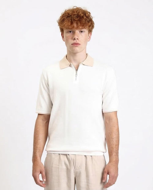 Person wearing a white polo shirt with a light-colored collar on a plain background