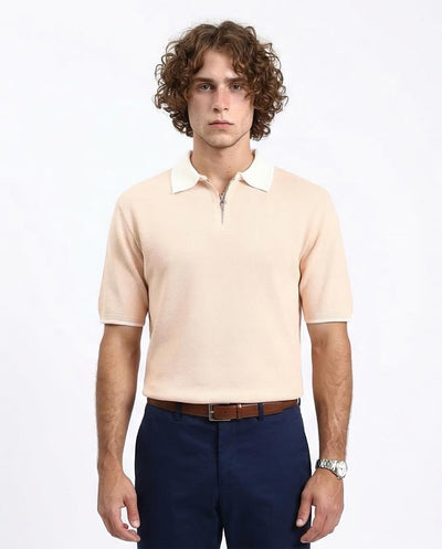 Man wearing a beige polo shirt with white collar and navy pants on a white background