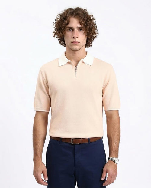 Man wearing a beige polo shirt with white collar and navy pants on a white background