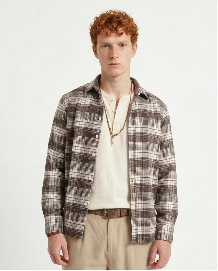 Man wearing a plaid shirt over a white shirt on a plain background