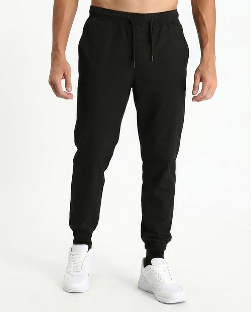 Person wearing black jogger pants and white sneakers on a white background