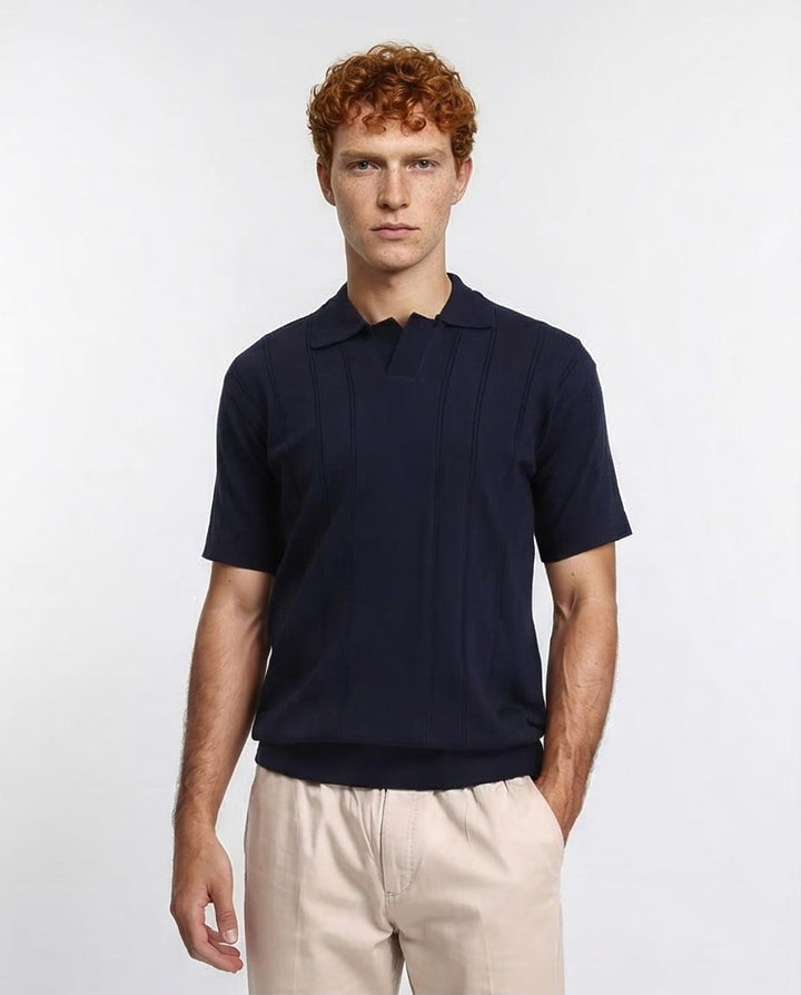 Man wearing a navy blue polo shirt and beige pants on a white background
