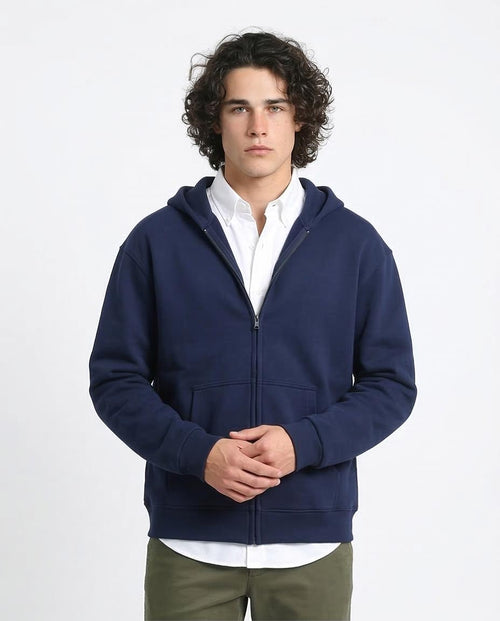 Man wearing a navy blue hoodie over a white shirt on a light gray background