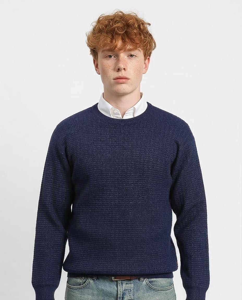 Man wearing a navy blue sweater over a white shirt on a light gray background