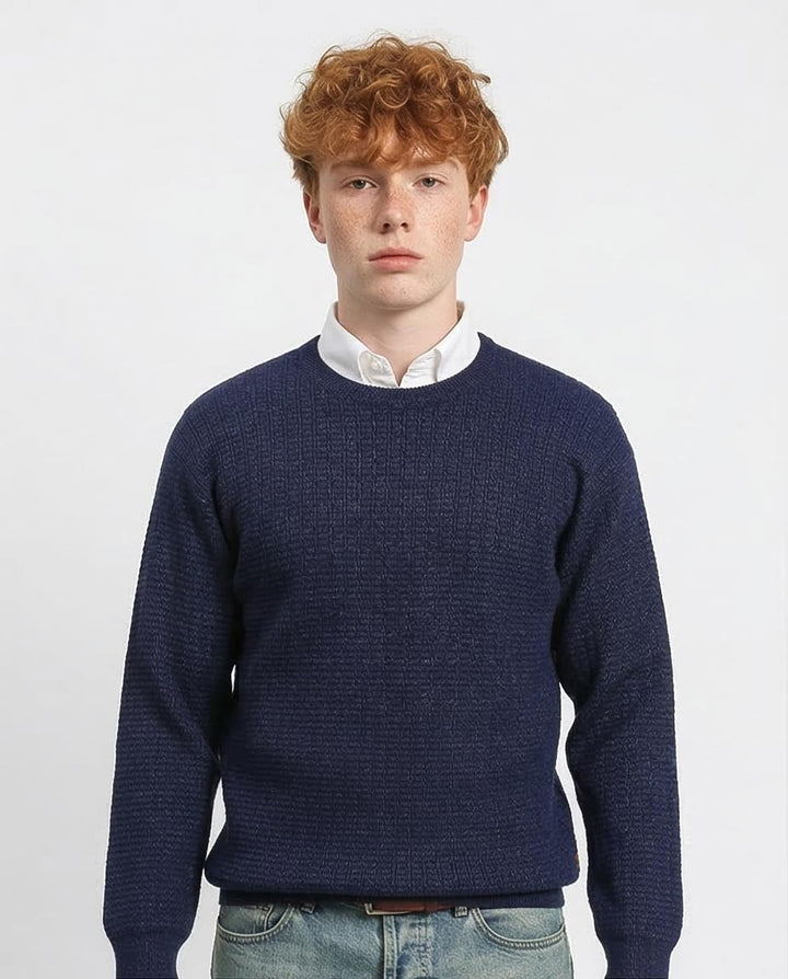Man wearing a navy blue sweater over a white shirt on a light gray background