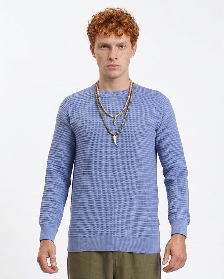 Man wearing a blue textured sweater and green pants on a white background