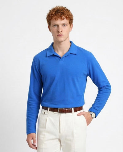 Man wearing a blue long-sleeve polo shirt and white pants on a light gray background