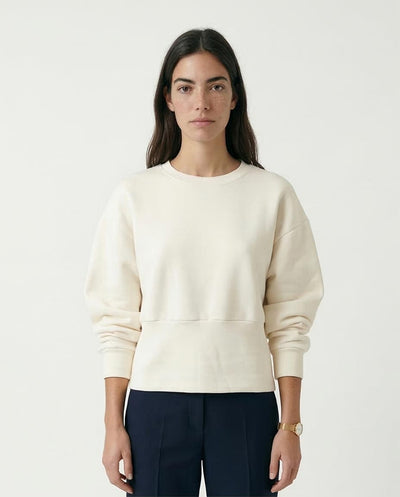 Woman wearing a cream sweater and dark pants on a white background