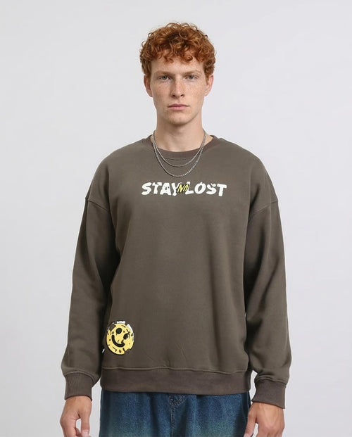 Person wearing a brown sweatshirt with 'STAY LOST' text on a plain background