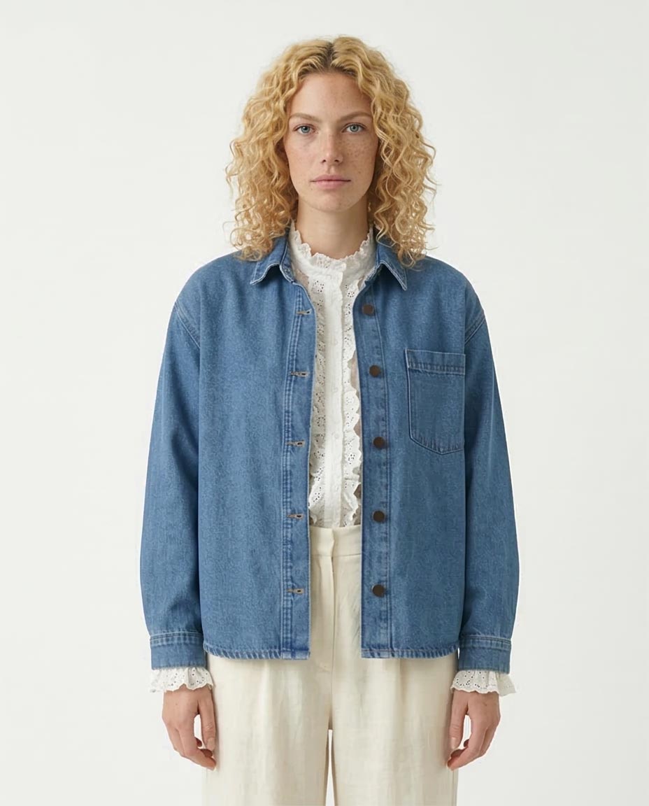 Woman wearing a blue denim jacket over a white top on a plain background
