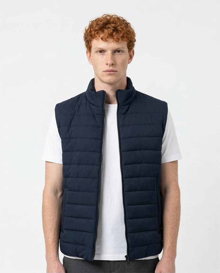 Man wearing a navy puffer vest over a white shirt on a light gray background
