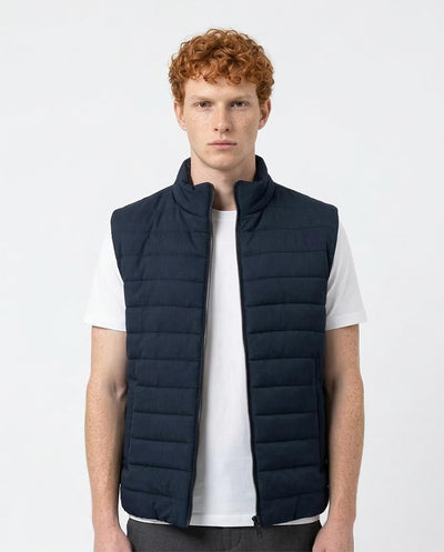 Man wearing a navy puffer vest over a white shirt on a light gray background