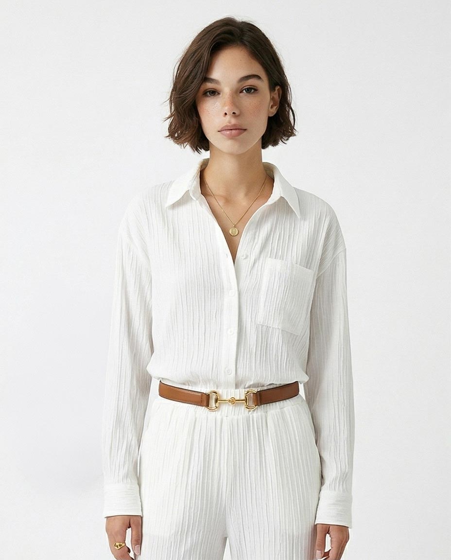 Woman wearing a white pleated shirt and pants with a brown belt on a white background