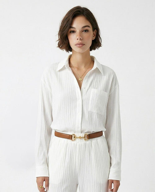 Woman wearing a white pleated shirt and pants with a brown belt on a white background
